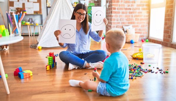 Young therapist woman speaking with child, counselor and behaviour correction at the office showing happy and sad face